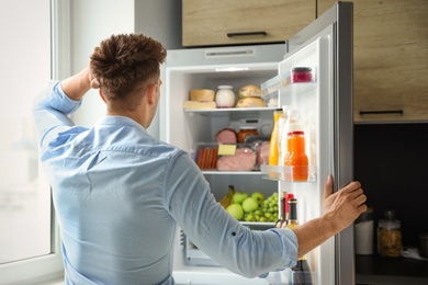 Photo of Man looking into refrigerator full of products in kitchen