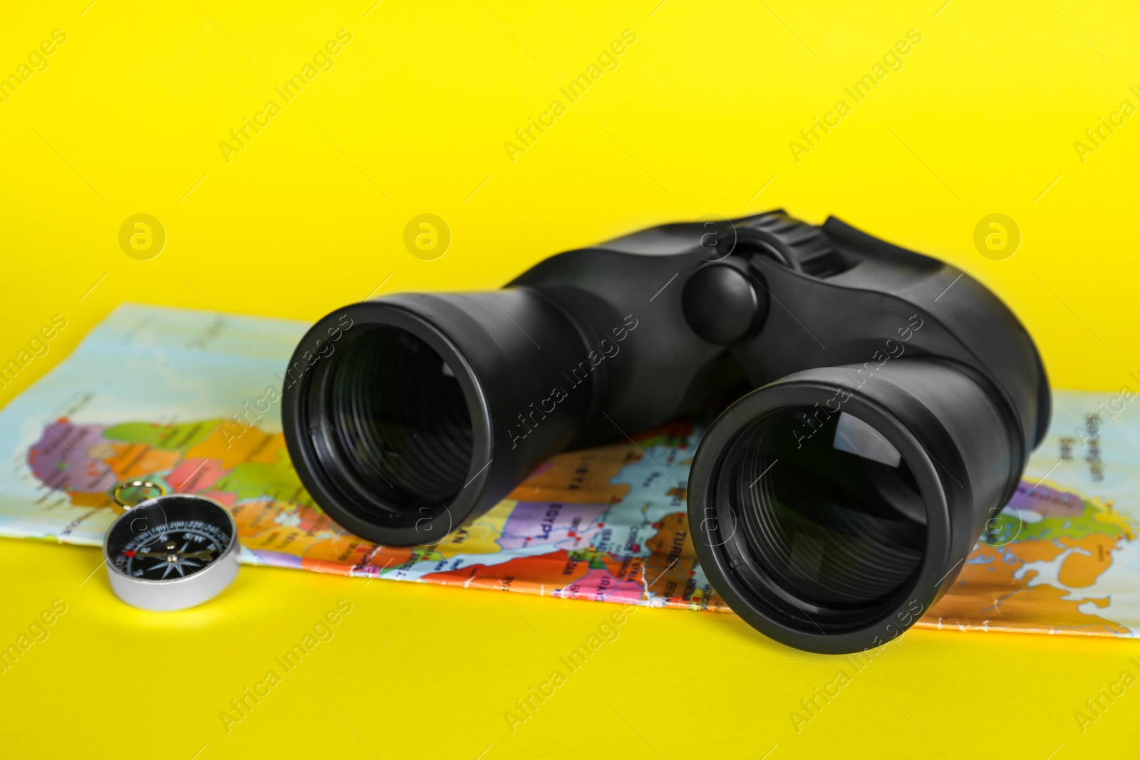 Photo of Modern binoculars, compass and map on yellow background, closeup