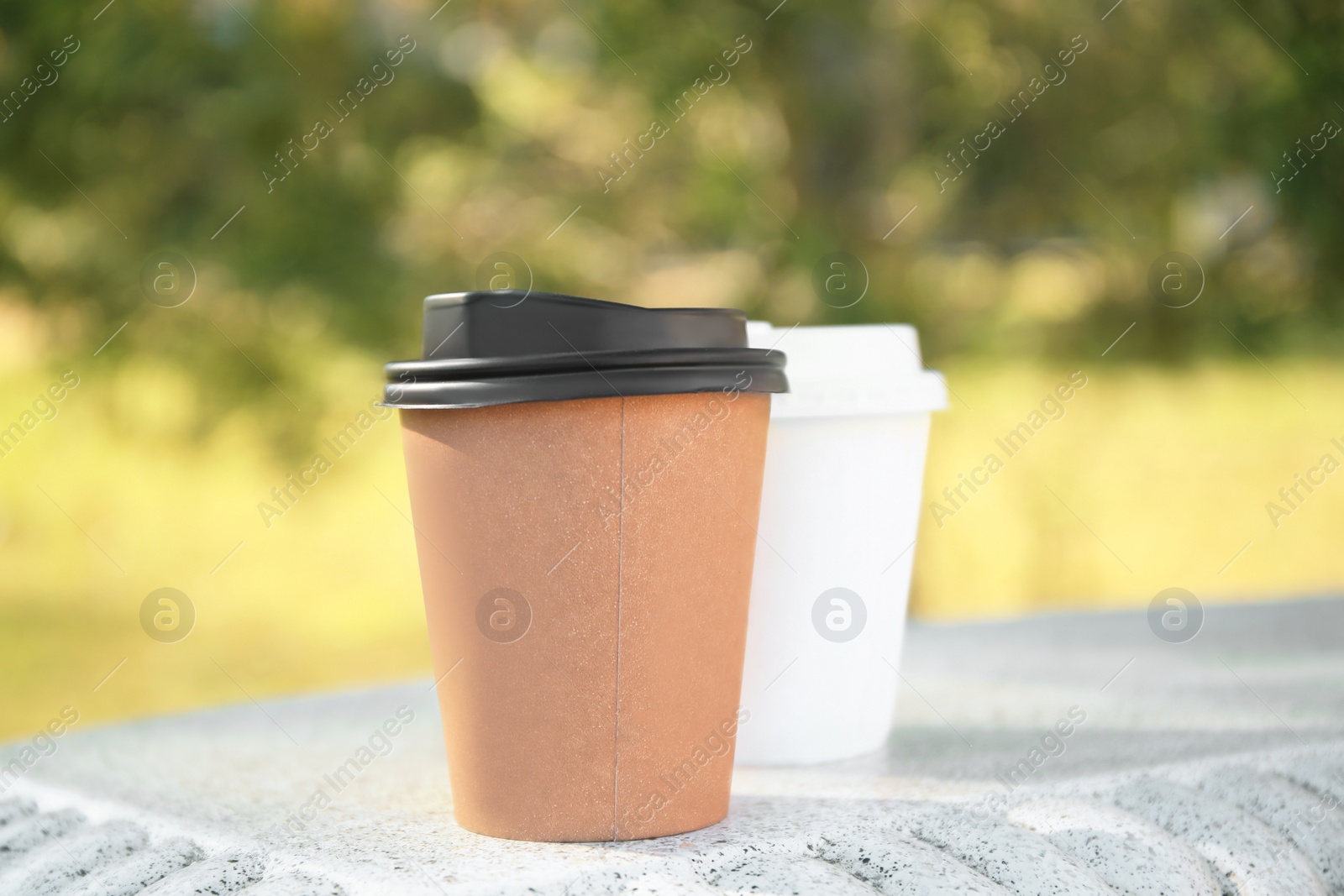 Photo of Cardboard cups with tasty coffee on stone bench outdoors, closeup