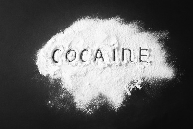 Heap of white powder with written word Cocaine on black background, top view