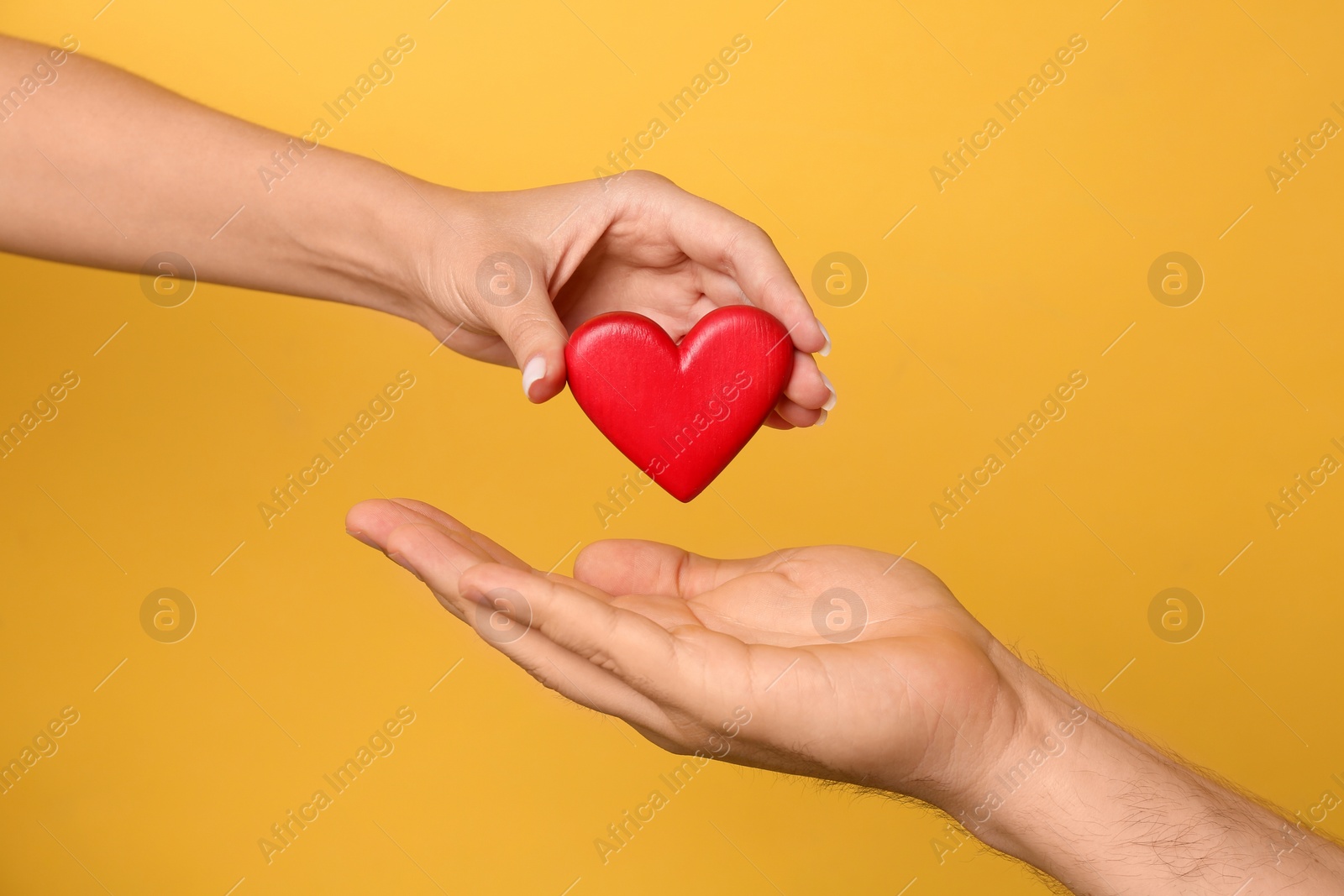 Photo of Woman giving red heart to man on yellow background, closeup. Donation concept