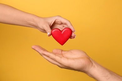 Photo of Woman giving red heart to man on yellow background, closeup. Donation concept