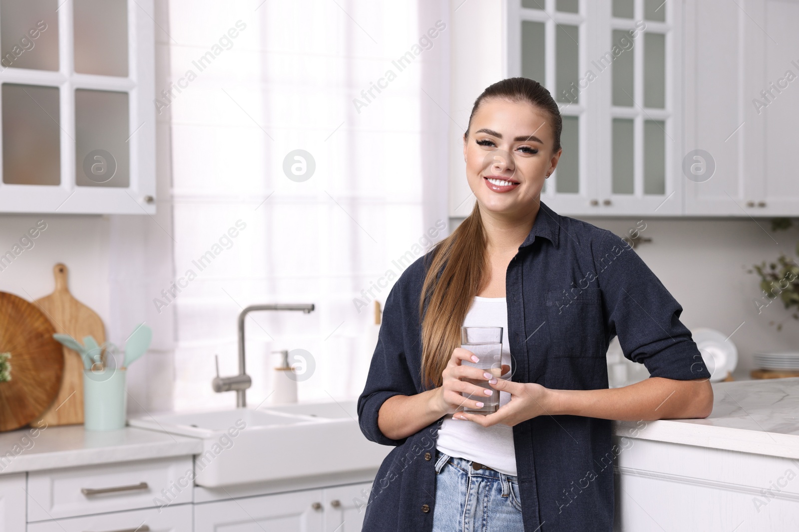Photo of Happy woman with glass of fresh water in kitchen, space for text