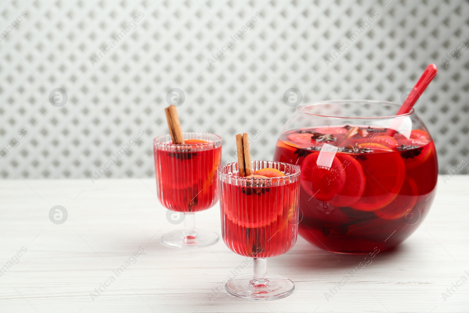 Photo of Glasses and bowl of delicious aromatic punch drink on white wooden table. Space for text