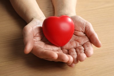 Photo of Elderly woman holding red heart in hands at wooden table, closeup