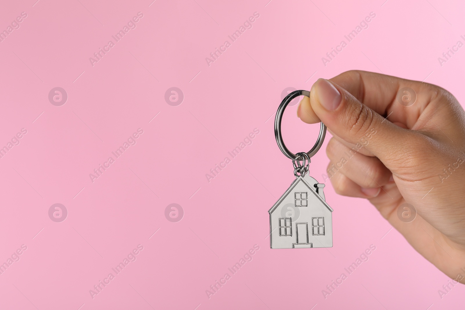 Photo of Woman holding metallic keychain in shape of house on pink background, closeup. Space for text