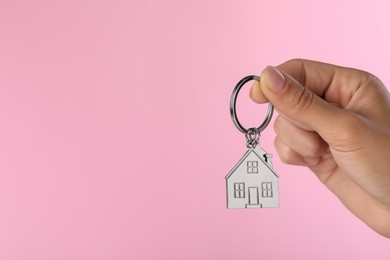 Woman holding metallic keychain in shape of house on pink background, closeup. Space for text