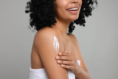 Photo of Young woman applying body cream onto shoulder on grey background, closeup