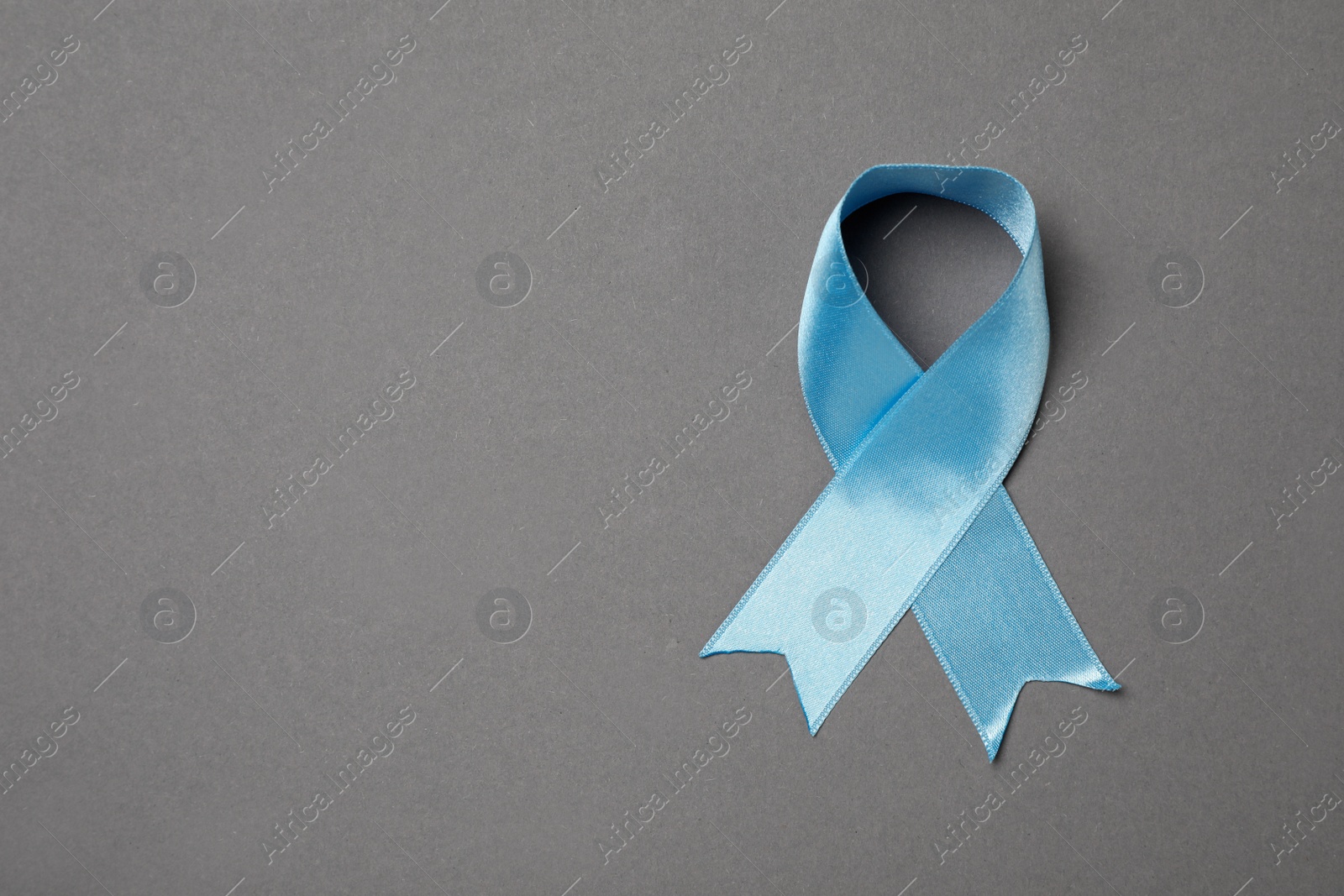 Photo of Light blue awareness ribbon on grey background, top view. Space for text