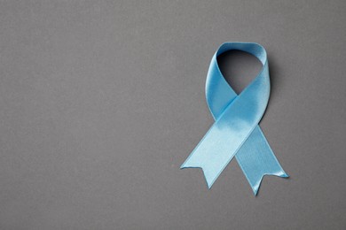 Photo of Light blue awareness ribbon on grey background, top view. Space for text