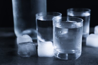 Photo of Shot glasses of vodka with ice on dark table, closeup