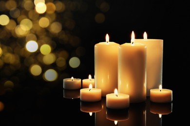 Image of Different wax candles burning on table against dark background with blurred lights. Bokeh effect