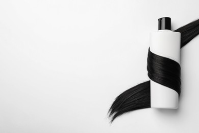 Photo of Shampoo bottle wrapped in lock of hair on white background, top view. Space for text