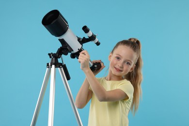 Photo of Happy little girl with telescope on light blue background