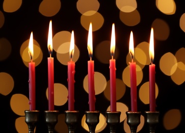 Golden menorah with burning candles against dark background and blurred festive lights