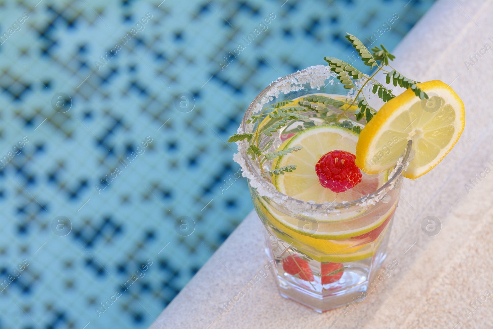 Photo of Delicious refreshing lemonade with raspberries near pool, closeup. Space for text