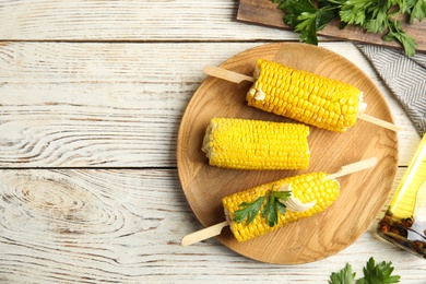 Photo of Fresh corn cobs with butter on white wooden table, flat lay. Space for text