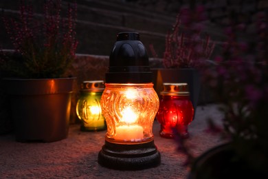 Photo of Different grave lanterns with burning candles on stone surface at night