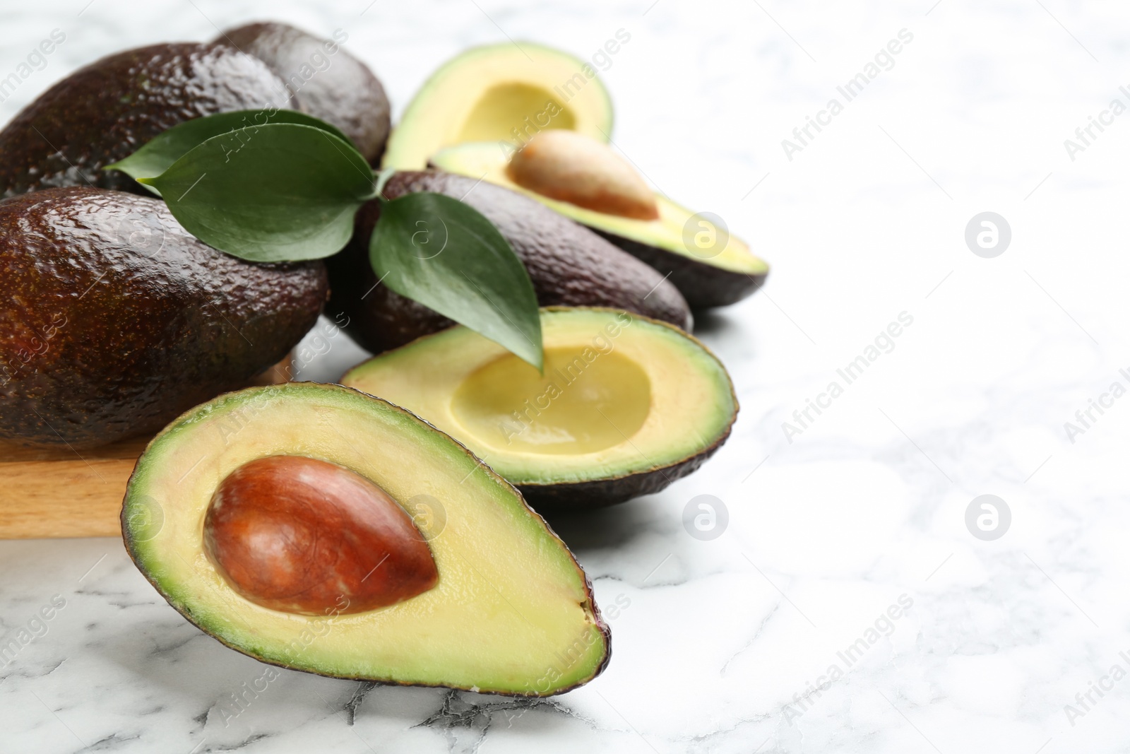 Photo of Whole and cut avocados with green leaves on white marble table. Space for text