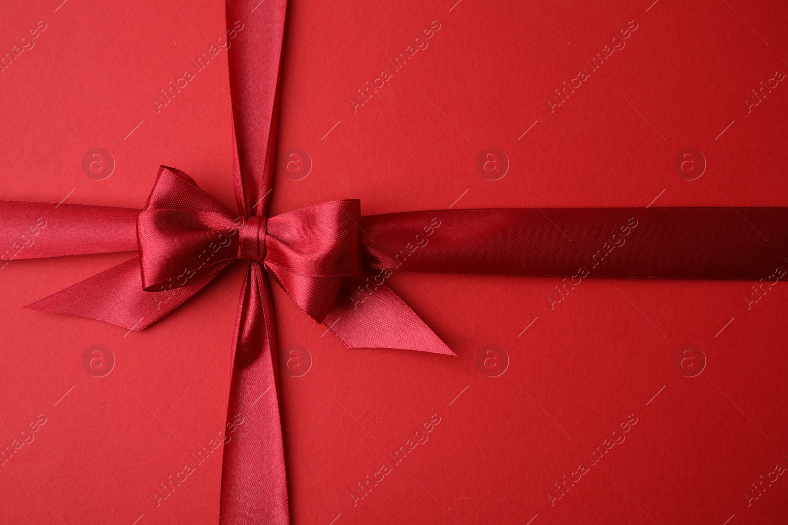 Photo of Bright satin ribbon with bow on red background, top view