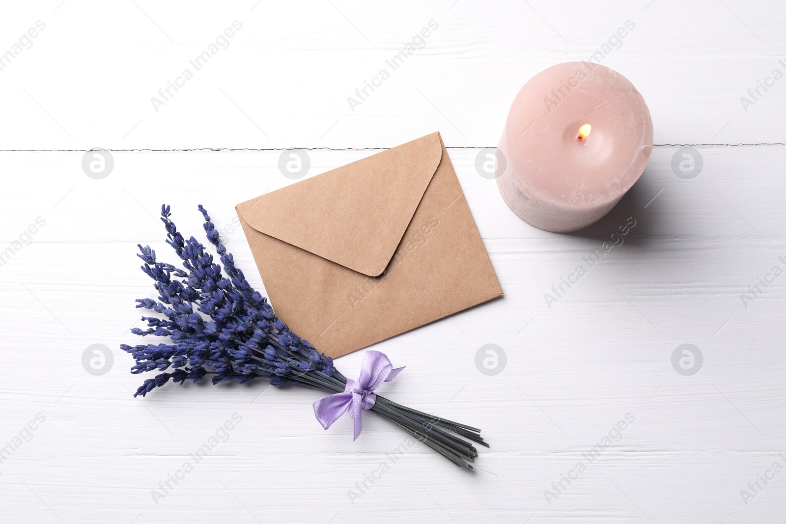 Photo of Bouquet of beautiful preserved lavender flowers, burning candle and envelope on white wooden table, flat lay