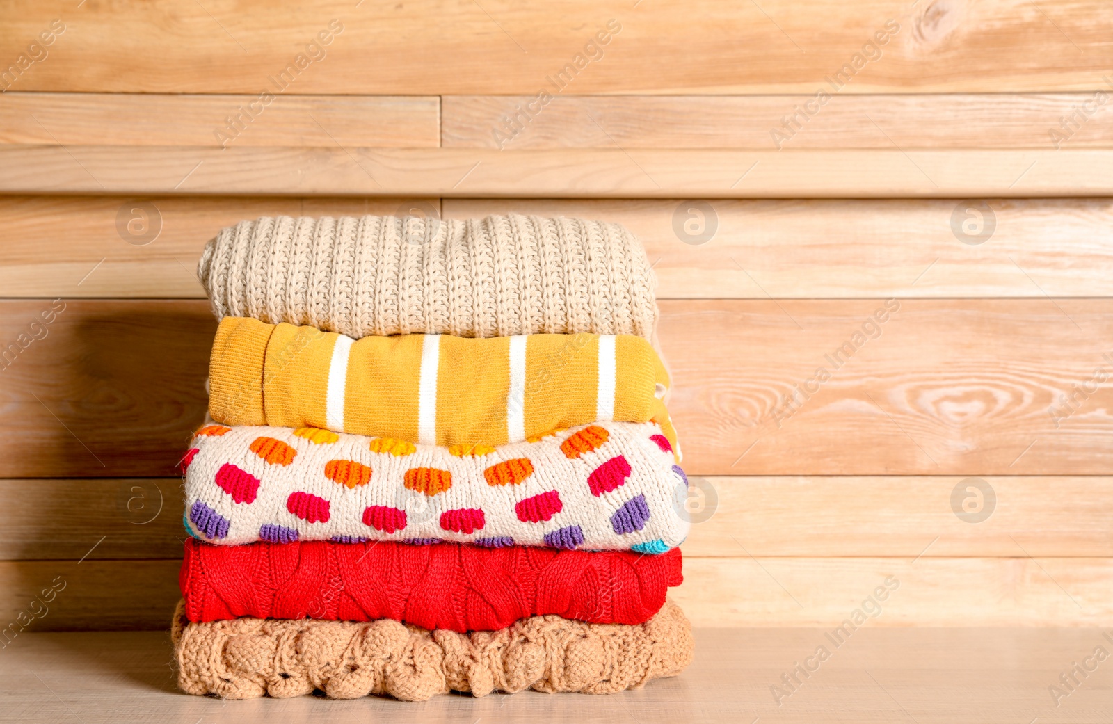 Photo of Stack of winter clothes against wooden background. Space for text