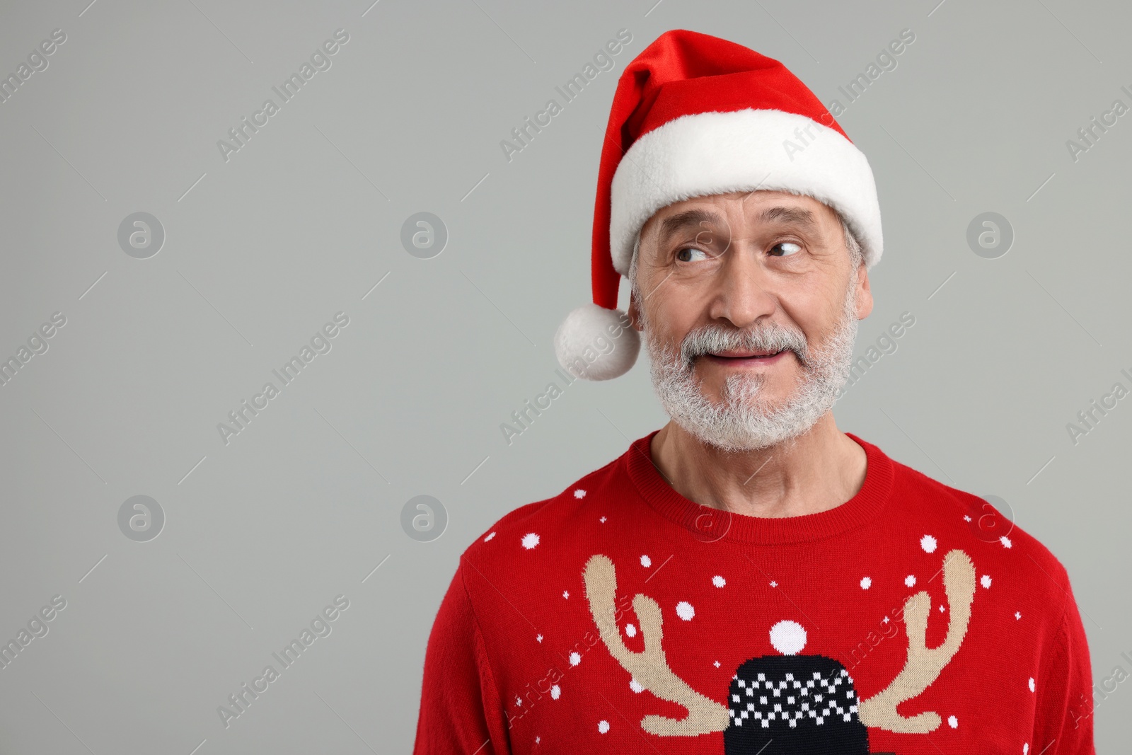 Photo of Senior man in Christmas sweater and Santa hat on grey background. Space for text
