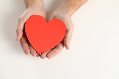 Man holding paper heart on white background, closeup