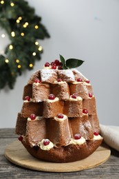 Delicious Pandoro Christmas tree cake with powdered sugar and berries near festive decor on wooden table