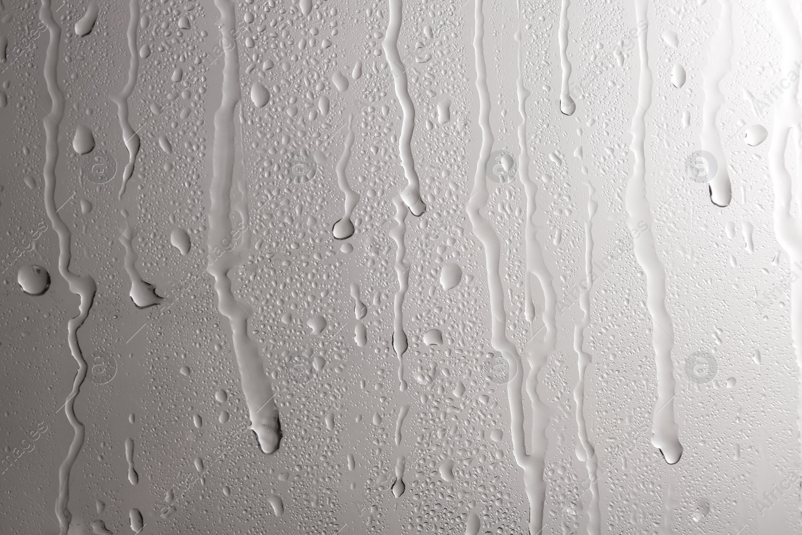 Photo of Glass with rain drops against light background