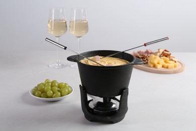 Photo of Fondue pot with tasty melted cheese, forks, wine and different snacks on white table