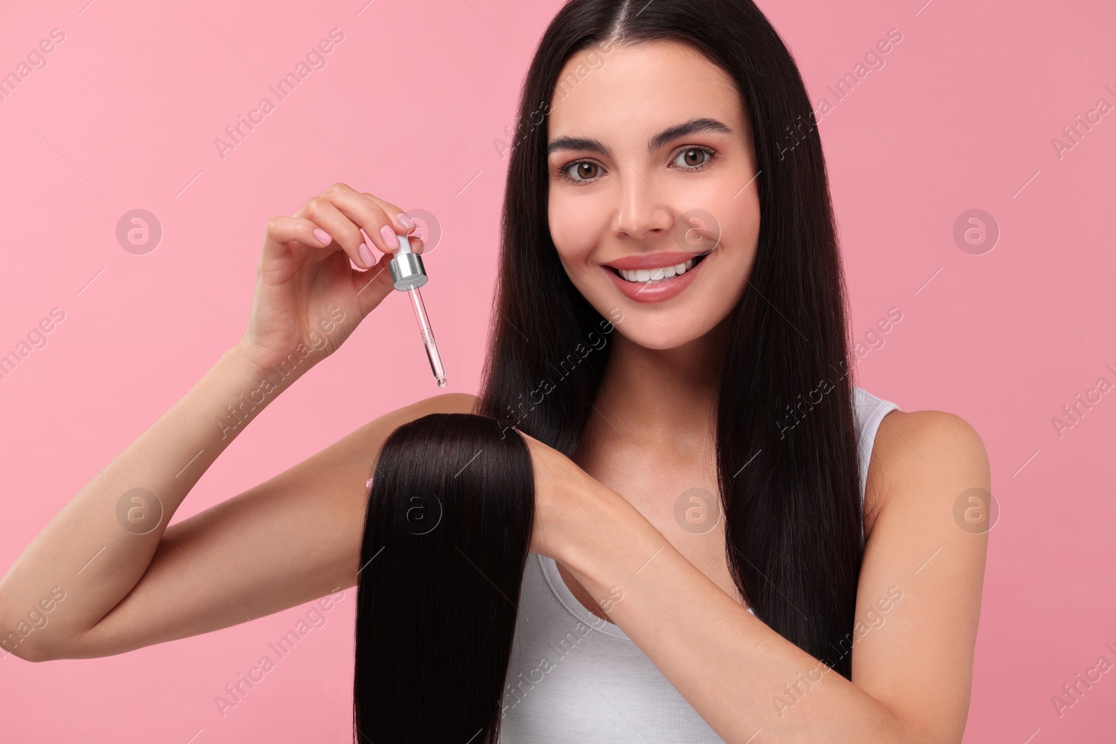 Photo of Beautiful woman applying hair serum on pink background. Cosmetic product