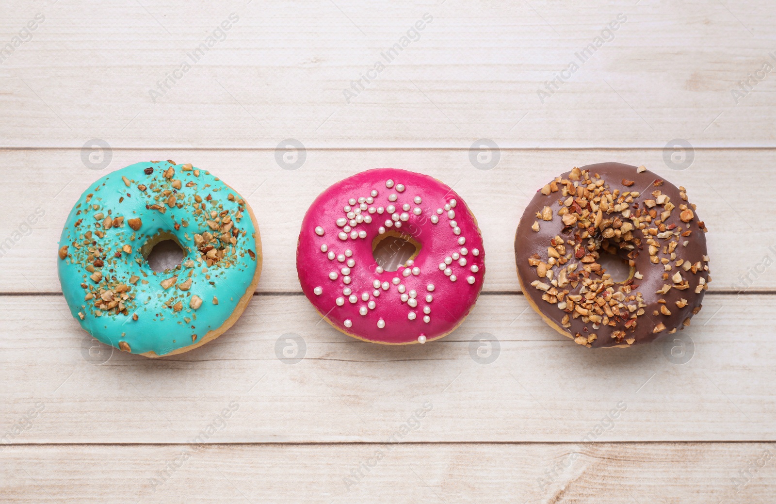 Photo of Tasty glazed donuts on white wooden table, flat lay