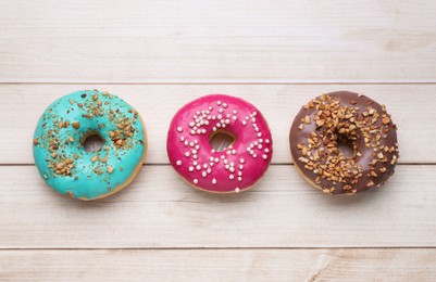 Photo of Tasty glazed donuts on white wooden table, flat lay