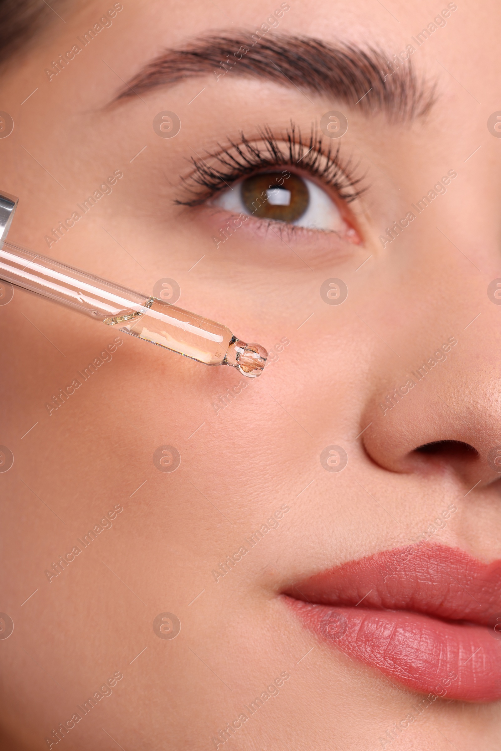 Photo of Young woman applying essential oil onto face, closeup