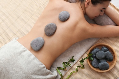 Photo of Beautiful young woman getting hot stone massage in spa salon, top view