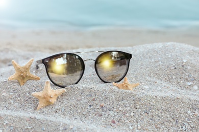 Stylish sunglasses and starfishes on sandy beach