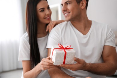 Photo of Man presenting gift to his beloved woman at home, focus on box. Valentine's day celebration