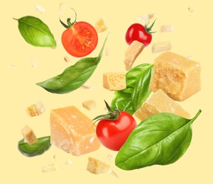 Image of Pieces of delicious parmesan, tomatoes and basil leaves falling on yellow background