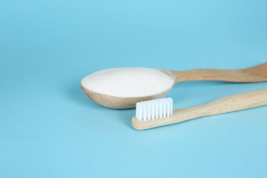 Photo of Bamboo toothbrush and wooden spoon with baking soda on light blue background