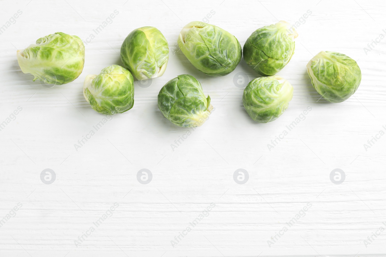 Photo of Fresh Brussels sprouts on white wooden table, flat lay. Space for text