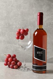 Photo of Bottle of delicious rose wine, glass and grapes on light grey table