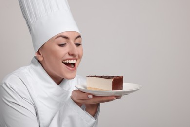 Photo of Happy professional confectioner in uniform holding delicious cheesecake on light grey background. Space for text