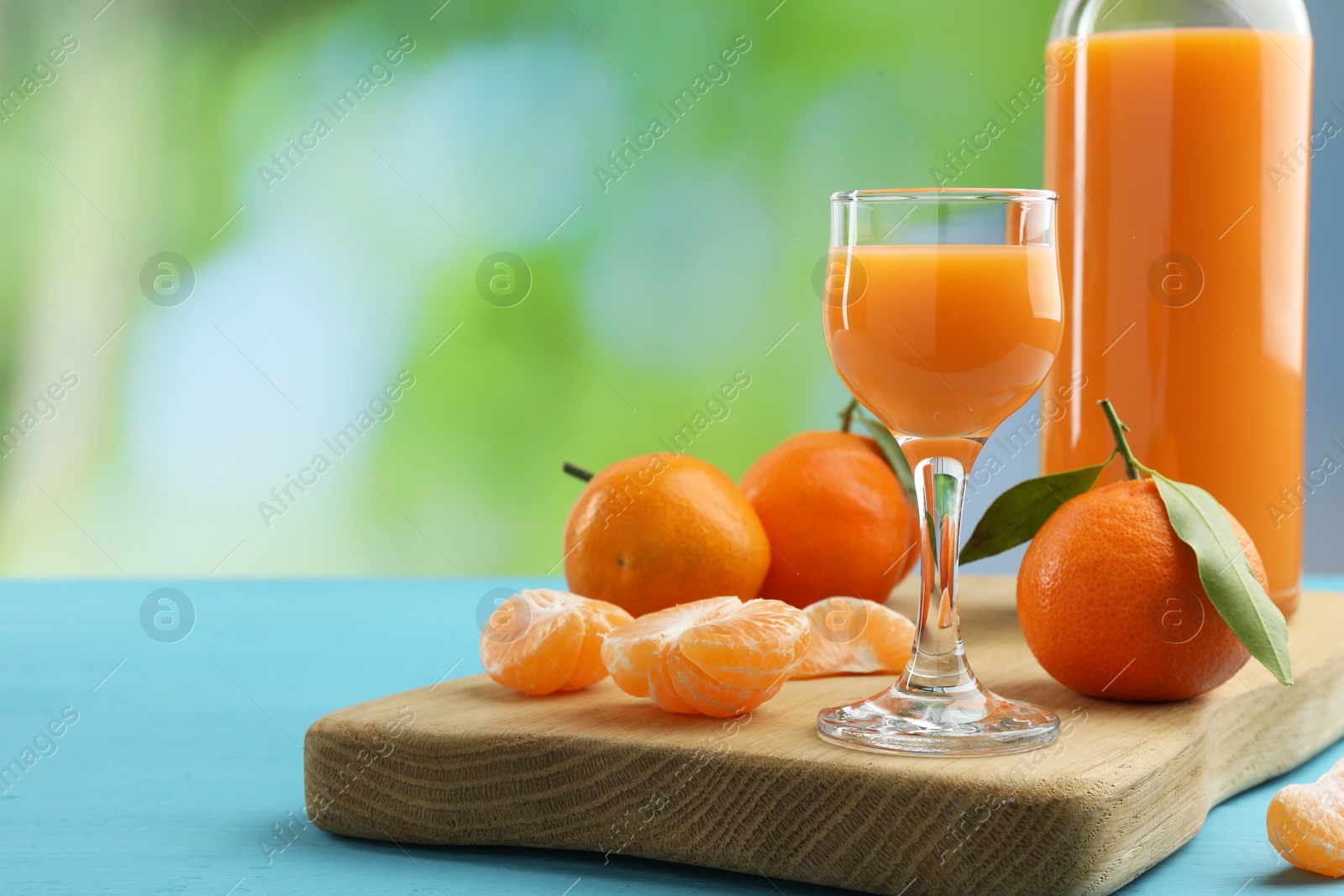 Photo of Delicious tangerine liqueur and fresh fruits on light blue wooden table, space for text