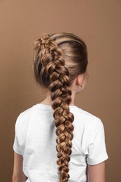 Little girl with braided hair on light brown background, back view