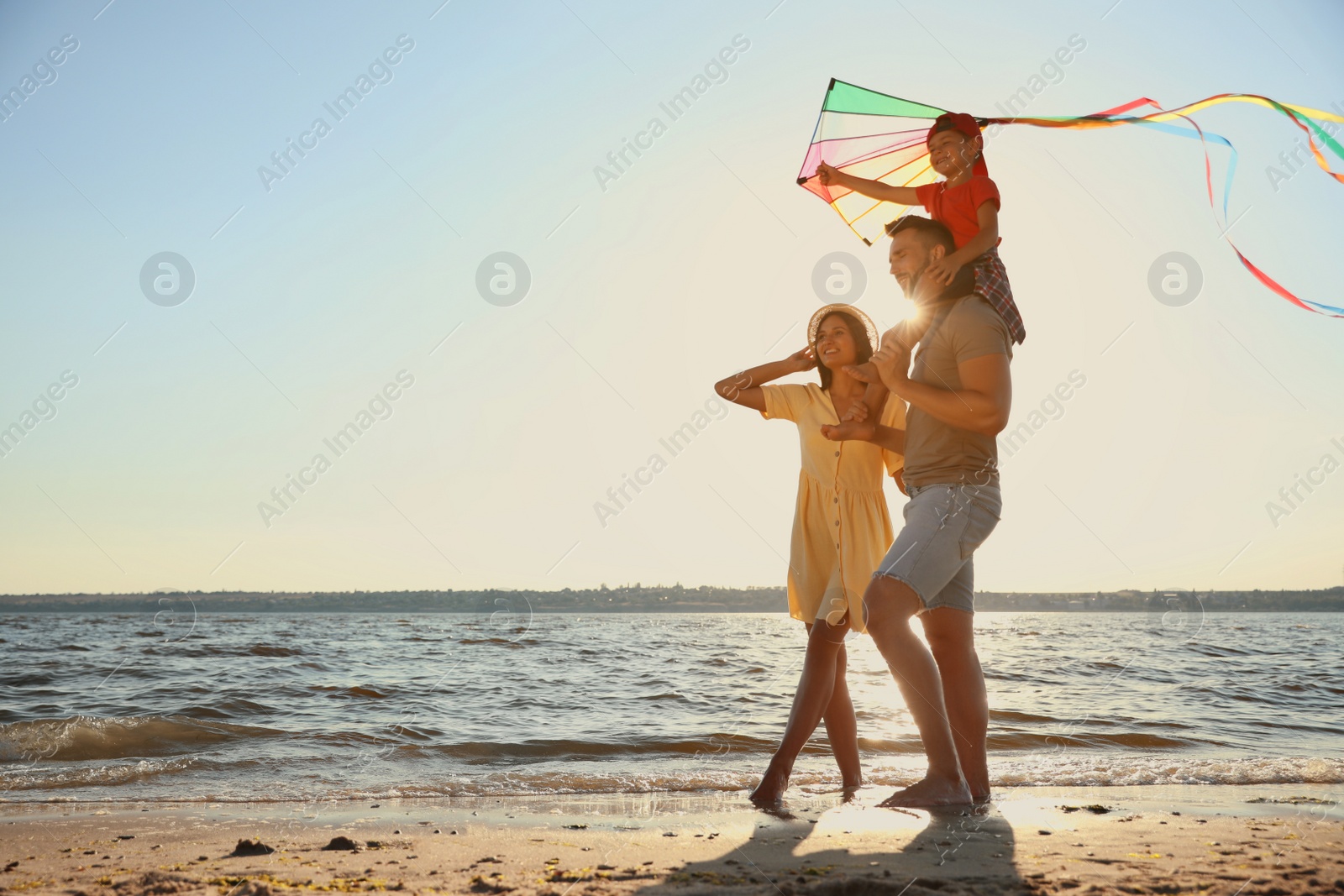 Photo of Happy parents and their child playing with kite on beach near sea. Spending time in nature