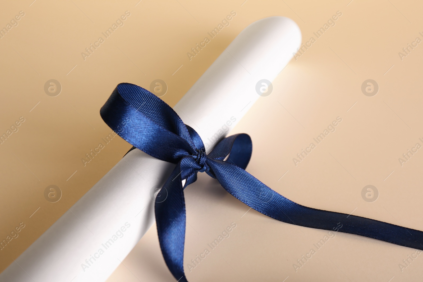Photo of Rolled student's diploma with blue ribbon on beige background, closeup