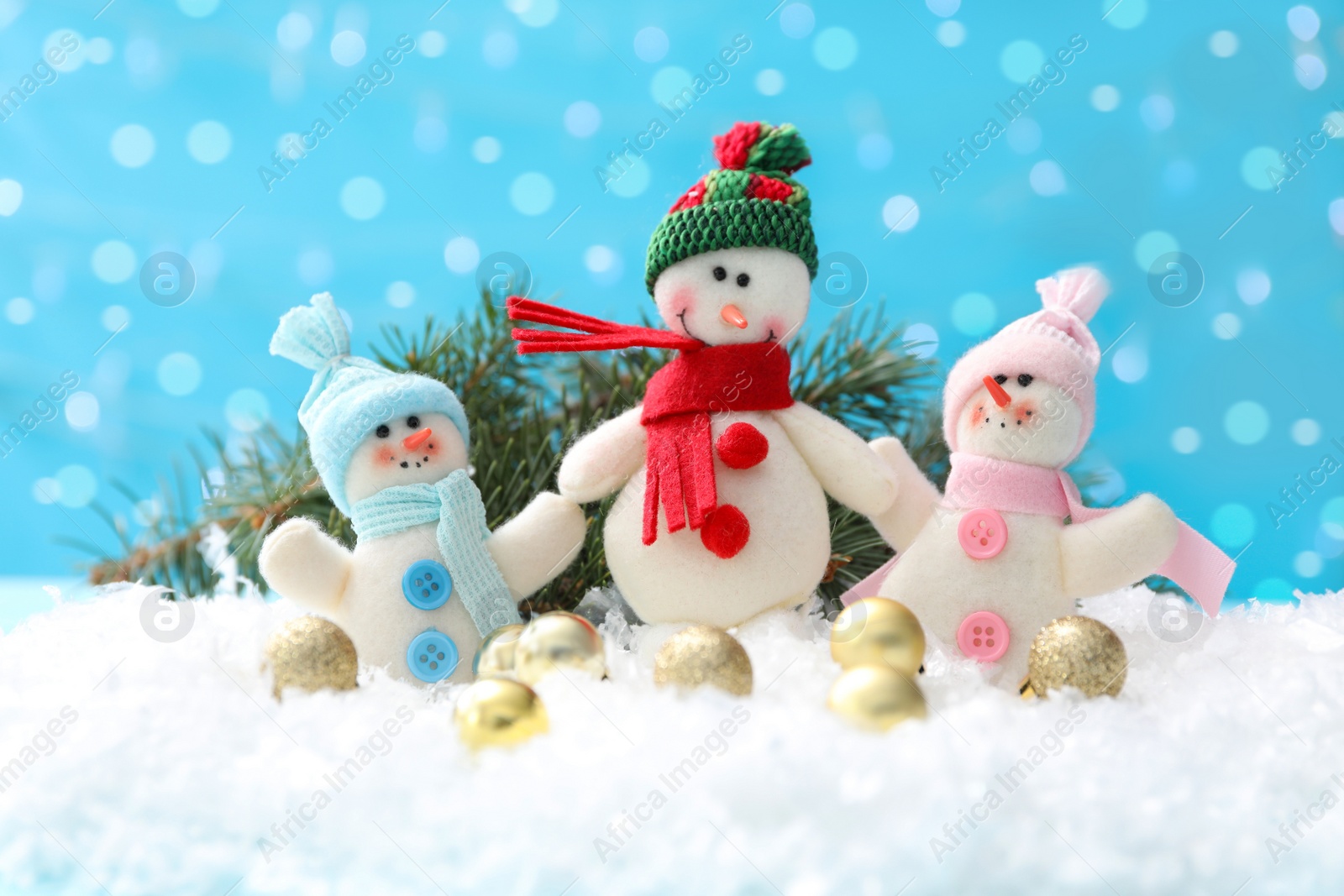Photo of Cute toy snowmen, fir branch and Christmas balls on snow against blurred background