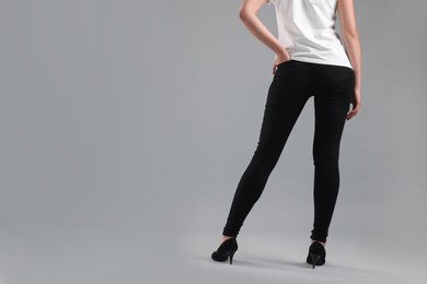 Woman wearing stylish black jeans and high heels shoes on light gray background, closeup. Space for text