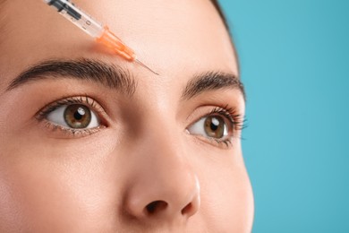 Young woman getting facial injection on light blue background, closeup. Cosmetic surgery